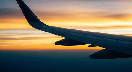 Obraz premium Commercial airplane wing in flight during a vivid golden and orange sunset with clear sky over the ocean, symbolizing journey and travel.