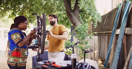 Healthy determined multiracial pair in yard fixing damaged bike components with professional...