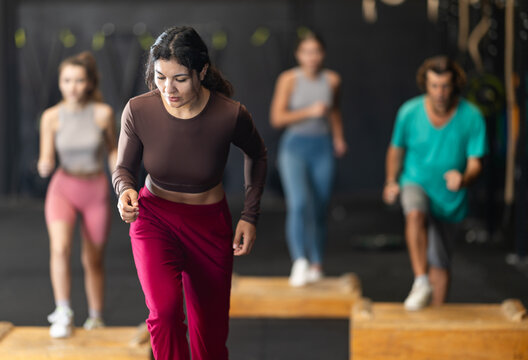 Sportive Latina girl doing step-up exercises with wooden box during crossfit workout in group - Powered by Adobe
