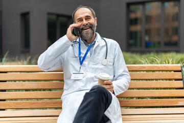 Senior doctor laughing talking on phone during coffee break