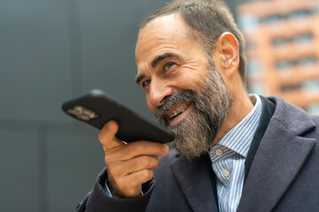 Mature man smiling using smartphone for voice message