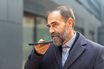Mature businessman using voice assistant on smartphone outdoors