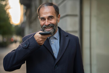 Bearded man smiling using smartphone voice command outdoors
