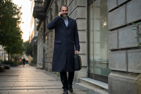 Mature businessman walking city street talking on phone