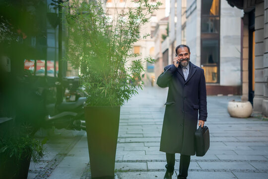 Mature businessman walking street talking on phone