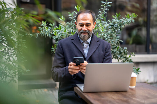 Mature businessman checking smartphone and working on laptop outdoors