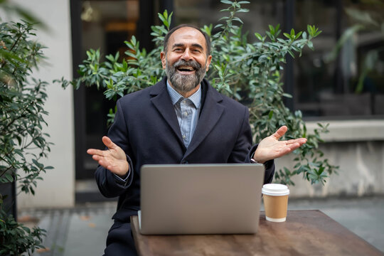 Happy mature man laughing opening hands outdoor cafe