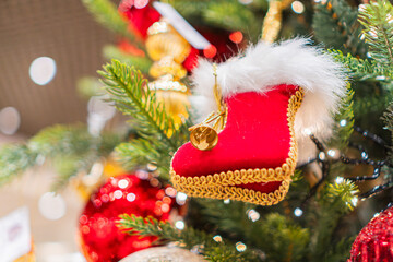 Close-up of a decorated Christmas tree branch with a plush, detailed red boot ornament, surrounded by spherical red and gold ornaments Realistic style photography capturing intricate details under e
