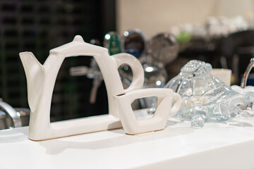 Modern ceramic teapot with geometric design, HA handle and spout, sharing space with a glass jar and metal pitcher on a light countertop New Years Christmas decorations, toys hanging on the tree, f