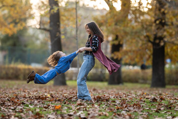 Mother and child playing, spinning with joy in autumn park