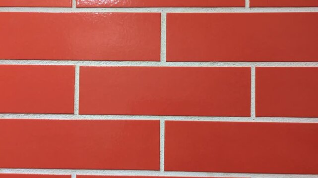 Close-up of a brick wall pattern made of orange or reddish rectangular tiles with white grout lines. The tiles are arranged in a staggered running bond pattern, giving a clean, uniform, and modern loo