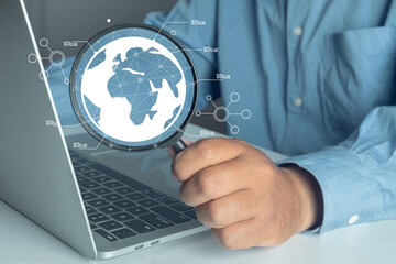 Businessman using magnifying glass on laptop to analyze global data. Global business, market research, international network, and strategy concept. Business Intelligence (BI).