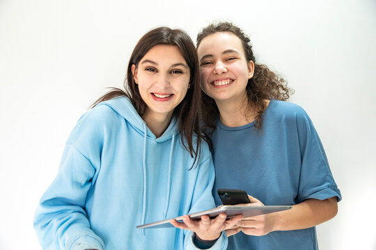 Friends enjoying technology while studying together indoors. Girls with gadgets