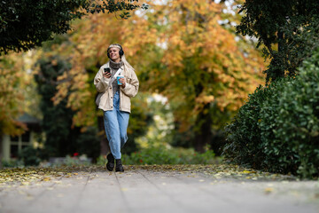 Fototapeta premium Young woman walking in park listening to music