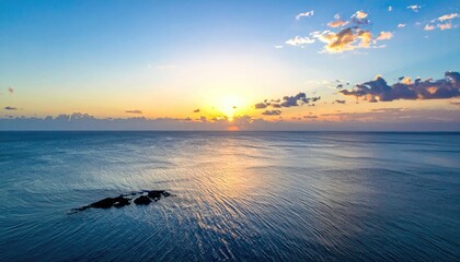 Aerial perspective of an ocean horizon at dawn. Sun breaks through clouds, casting rays on the rippled water. Small island present