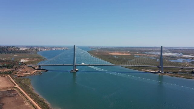 Wide aerial view of Guadiana International Bridge spanning river between Spain and Portugal with visible wetlands and clear blue sky. Concept of European cooperation and cross-border infrastructure