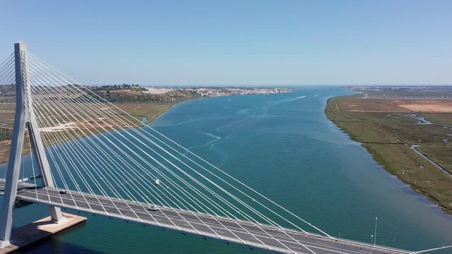 Ponte internacional Guadiana aerial cable-stayed bridge over river, glassy turquoise water and marshland, towering pylon with radiating cables, drone perspective from portuguese bank