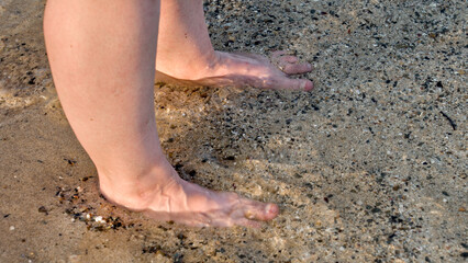 A pair of feet stand in the sand as gentle waves wash over them, creating a peaceful and refreshing beach moment.