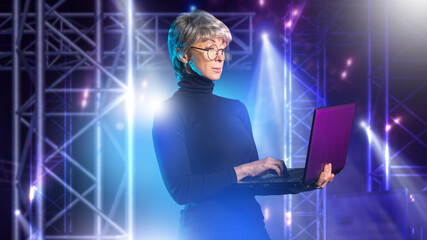 Stage lighting designer operates laptop, controlling illumination and effects during live performance setup in concert venue.