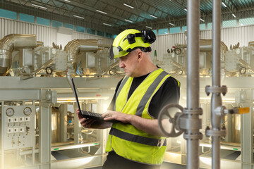 Industrial equipment maintenance technician checks process machinery using a laptop, controlling system parameters and overseeing mechanical operations in the plant.