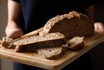 Dark rye sourdough bread topped with sesame seeds, a healthy vegetarian food, held in a woman's hand.