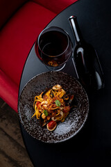 A vibrant plate of seafood pasta sits elegantly on a stylish black table, complemented by a glass of red wine. The cozy ambiance of the restaurant creates a perfect dining atmosphere