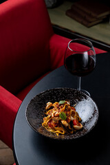 A beautiful bowl of pasta topped with seafood sits on a sleek black table. A glass of red wine complements the dish. The vibrant red chair adds warmth to the cozy atmosphere