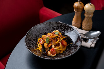 A mouthwatering plate of seafood pasta featuring mussels, calamari, and cherry tomatoes, beautifully arranged in a stylish black bowl. The chic red background adds warmth, perfect for a cozy dinner