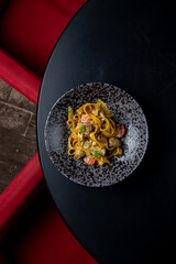 A colorful plate of pasta with vibrant vegetables is elegantly displayed on a dark table. Red surroundings create a warm ambiance for a delightful dining experience