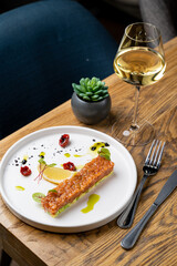 A beautifully plated seafood dish sits on a white plate, garnished with colorful toppings. Next to it, a glass of white wine captures the restaurant's cozy ambiance