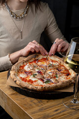 A guest lovingly pulls apart a slice of delicious gourmet pizza topped with fresh ingredients while sipping a glass of white wine in a modern eatery