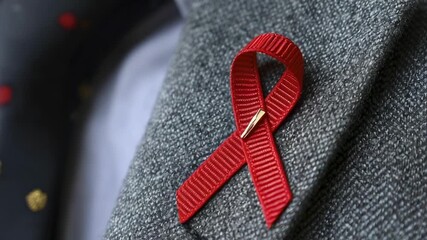 A close-up of a red awareness ribbon pinned to the lapel of a gray textured jacket