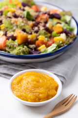 Healthy vegetable salad with lettuce, quinoa seed, azuki bean, corn, tomato, pumpkin and purple sweet potato in a bowl and pumpkin dressing on white background. Vegan and plant-based food