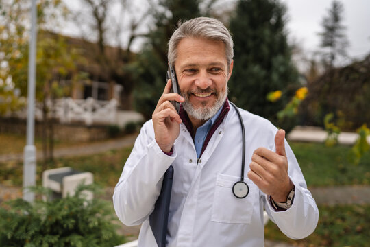 Smiling male doctor talking on phone outdoors