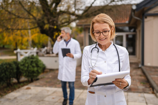 Experienced female doctor writing on clipboard outdoors