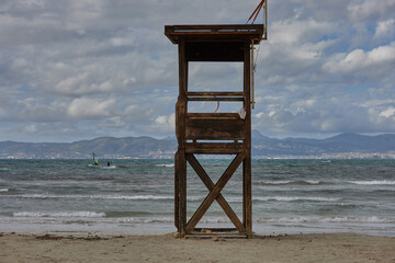 Old wooden lifeguard tower on a quiet sandy beach, with waves rolling in and mountains visible in the distant background. lifeguard, beach