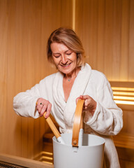Senior woman enjoying sauna pouring water on hot stones