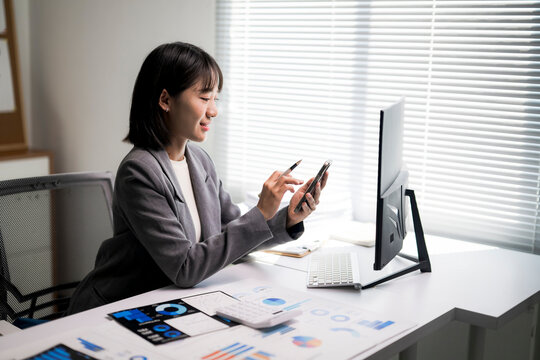 Asian businesswoman analyzing data using smartphone at desk