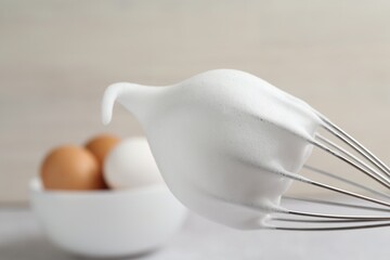 Whisk with whipped egg whites on blurred background, closeup. Space for text