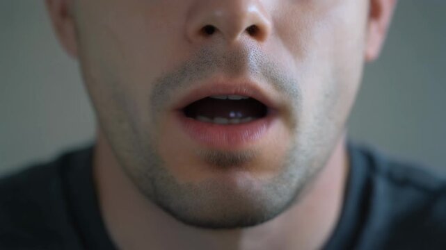 Close-up shot of a man's mouth slightly open, as if speaking or singing, showing his chin and stubble.