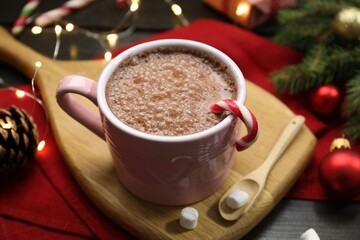 Tasty hot cocoa drink with candy cane in cup, marshmallows and Christmas decor on dark wooden table, closeup
