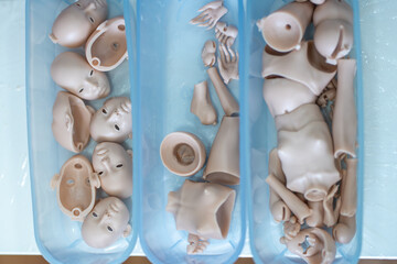 Multiple unassembled ball jointed doll head and body parts organized in blue trays showing preparation stage for artisan doll assembly and creative manufacturing