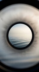 A view through a circular porthole showing calm water and a soft sky, creating a tranquil and scenic perspective of the ocean or lake surface
