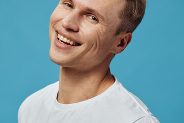 Obraz premium Smiling man with short brown hair wearing a white t-shirt looking at camera isolated on a plain turquoise background for lifestyle, portrait, happiness, facial expression, casual clothing, people