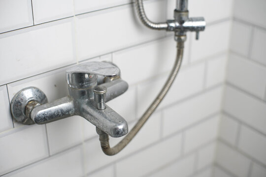 Old, corroded shower mixer tap with limescale buildup on white subway tiles. Reflects plumbing issues, hard water damage, and renovation needs.