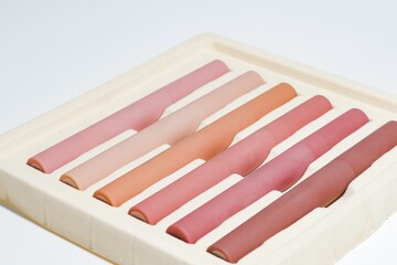 Fototapeta premium Gradient of nude and pink lipsticks in a sustainable packaging tray on a white background, ideal for beauty and cosmetic themes.