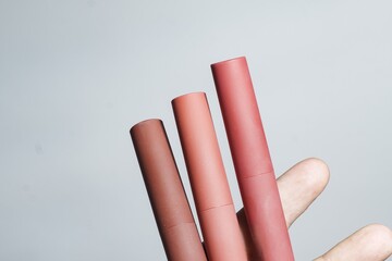 Three nude-to-pink matte liquid lipsticks held in a hand, showcasing diverse shades for beauty, cosmetics, and makeup concepts on a light background.