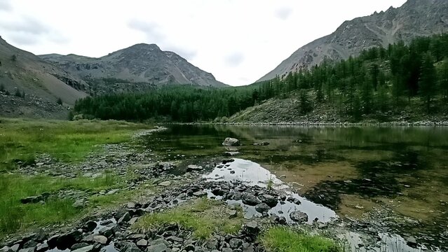 Reflection of mountain ranges in the calm surface of a beautiful shallow lake with emerald water, on a cloudy summer evening. - Powered by Adobe