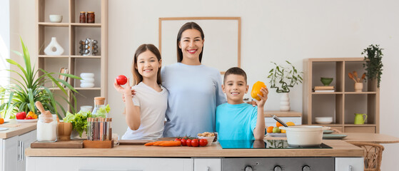 Young mother hugging her children with vegetables in kitchen