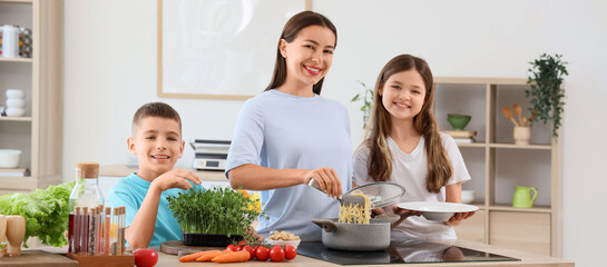 Young mother with her children putting tasty pasta onto plate in kitchen
